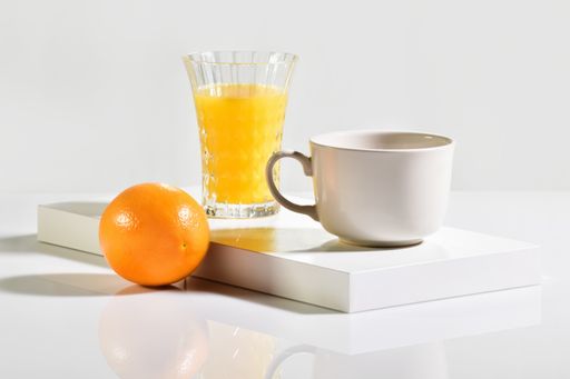 Close up of a cup next to a whole orange with a glass of orange juice behind on an out of focus light background. Breakfast and fruit concept.