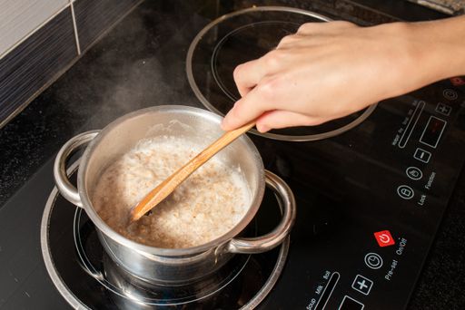 A high angle shot of a person cooking oatmeal with milk in a pot on the stove