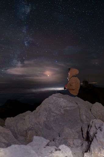 An adventurous man sitting on the rocks and looking at the night sky full of shining stars