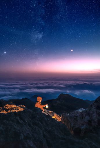 An adventurous man sitting on the rocks holding a lamp under the sunset in the sky full of stars