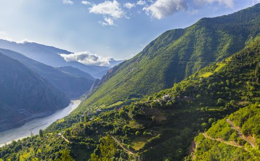A river surrounded by hills covered in forests under the sunlight and a blue sky