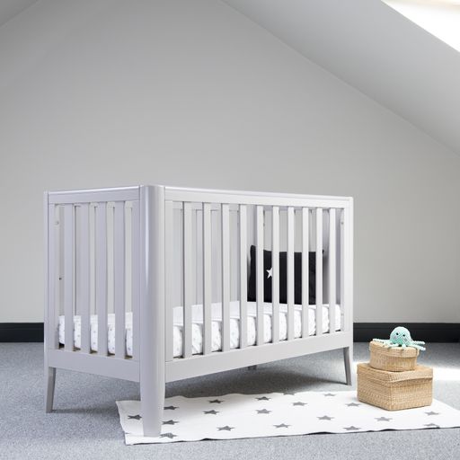 An interior of light baby room with a modern cozy crib and woven wicker boxes for clothes or accessories