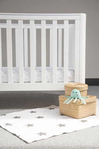 An interior of light baby room with a modern cozy crib and woven wicker boxes on a soft starry carpet
