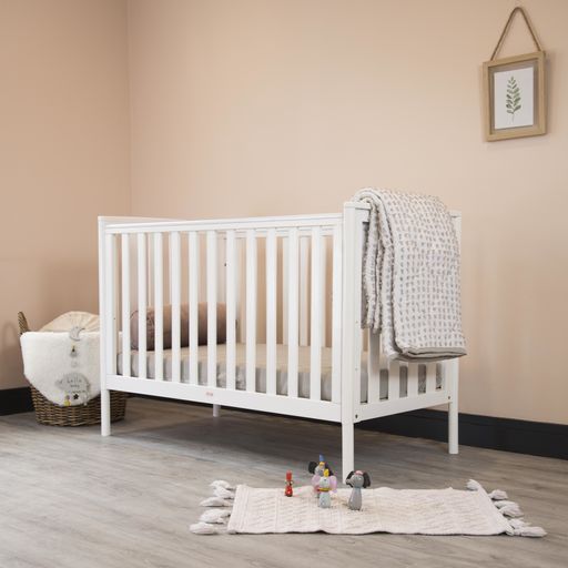 A cozy classic crib in a light baby room with toys on a soft carpet and a woven basket on the corner