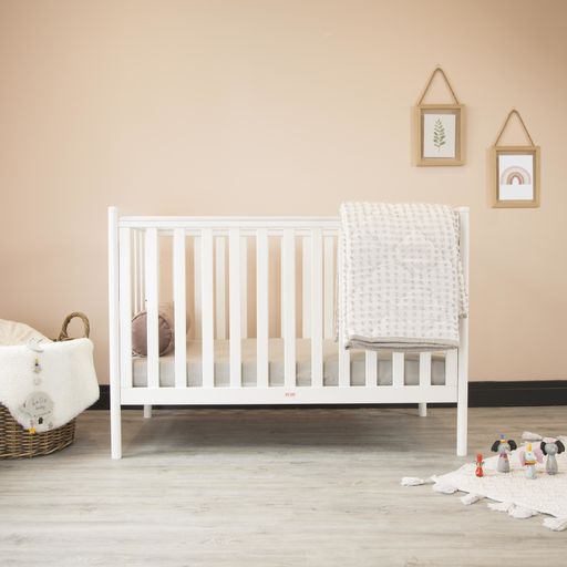 A cozy classic crib in a light baby room with toys on a soft carpet and a woven basket on the corner