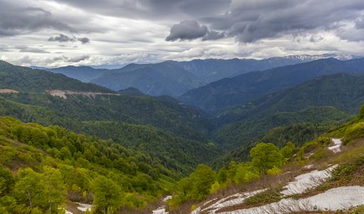 A landscape of hills covered in forests and snow under a dark cloudy sky