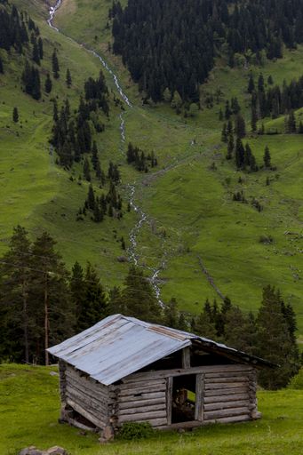 An old wooden barn surrounded by forests and rocks with the river on the background