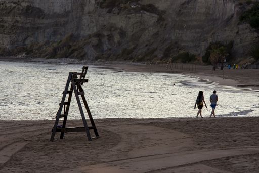 A view of the beach with a tower for a lifeguard, and a couple walking along the shore