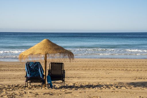 A beautiful view of sandy beach with a wooden umbrella and deck chairs