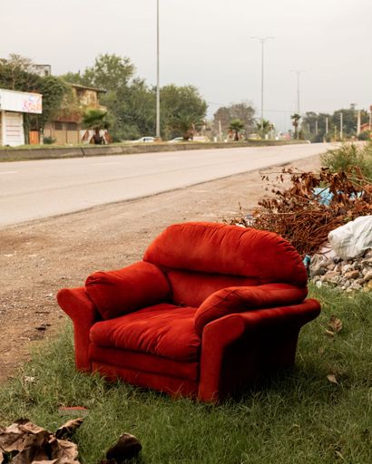 An abandoned red sofa, situated on a grassy area in a rural landscape
