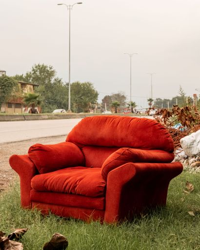An abandoned red sofa, situated on a grassy area in a rural landscape