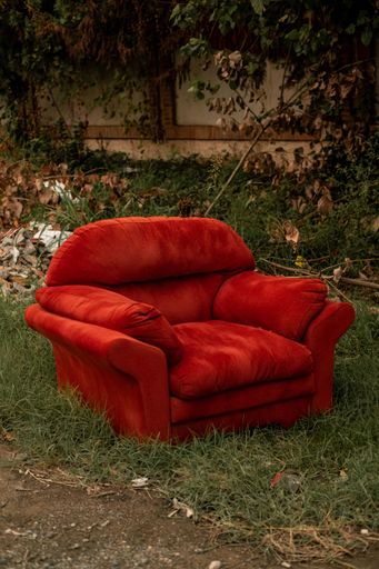 An abandoned red sofa, situated on a grassy area in a rural landscape