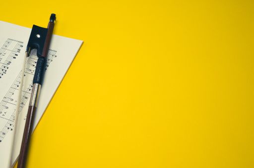 A closeup of a violin bow with sheet music on the yellow surface - space for text