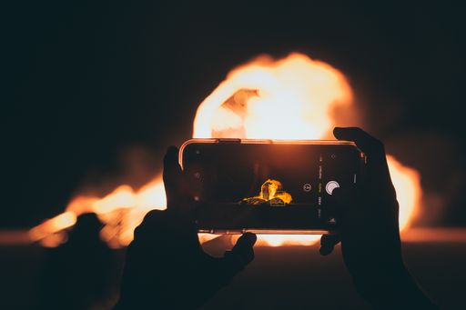 A person taking a picture of the bonfire with a smartphone at night time