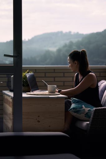 A beautiful young female working from home on the balcony on her laptop