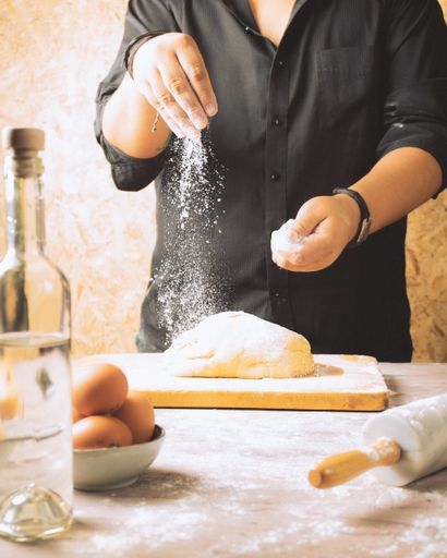A vertical shot of a baker mixing the dough with flour