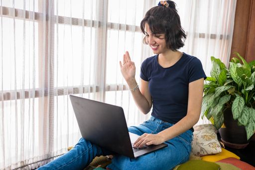 A Hispanic woman having a meeting on her computer while sitting on colorful cushions