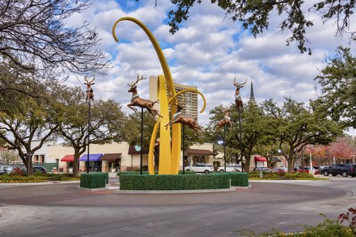 A picture of a yellow statue with brown deers around it surrounded by greenery under a cloudy sky