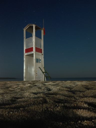 A vertical shot of a wooden lifeguard tower on an empty beach during a starry night