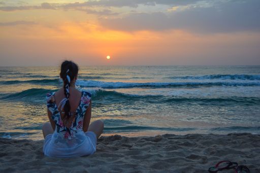 The view of a woman relaxing while sitting before the sea waves on the beach at sunset