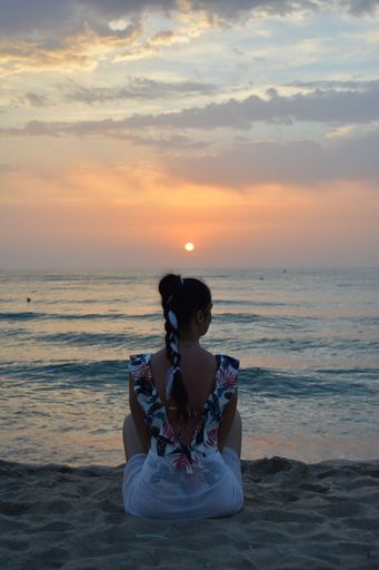 A relaxed young woman sits on a sun-drenched beach with her legs crossed, doing yoga