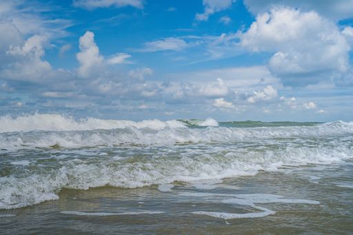 A beautiful shot of a wavy sea taken from a seashore under a cloudy blue sky