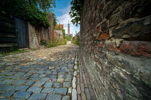 A high angle shot of a stoned alley surrounded by bricked walls with a tower in the background