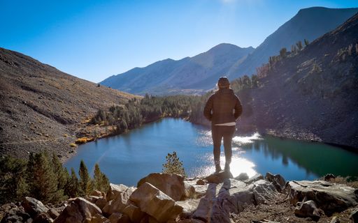 A solo female hiker stands on a rock promontory over Blue Lake in the Eastern Sierra's Virginia Lakes hiking area.