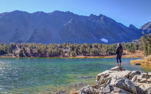 A female solo hiker stands at the edge of Frog Lakes, one of the alpine lakes in the Virginia Lakes area.