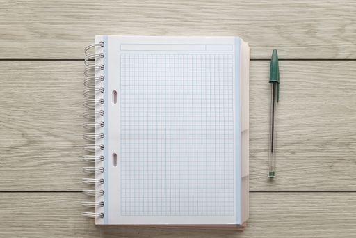 A high angle shot of a blank notebook and a green pen on a wooden surface