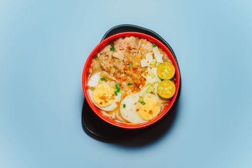 A top view of a delicious bowl of special Lomi with eggs and chicken isolated on a blue background