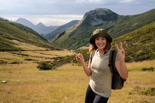 Young caucasian woman with a hat and a backpack making funny gestures while trekking in the nature.
