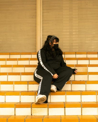 A closeup of a young Hispanic female with a spiked headband wearing a black medical sitting on the stairs