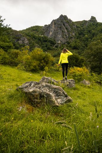 a vertical shot of a Young woman scouting over a rock toward the mountains in Asturias