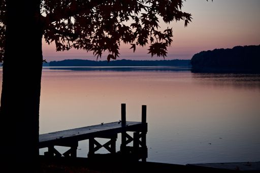 A vertical shot of a wooden pontoon against a lake from shore at sunset