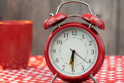 A closeup shot of a red alarm clock with a cup of coffee in the blurred background for the morning