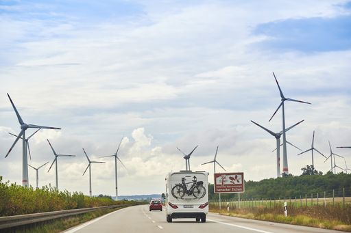 Camper on the freeway 20 with a bike carrier attached to the stern and bicycles mounted on it. Near the freeway you can see wind turbines.