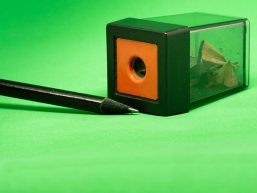 A closeup shot of a pencil and a sharpener on a green surface