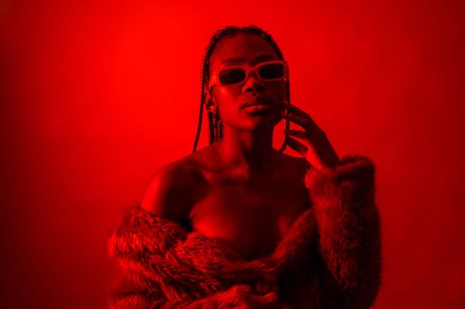 A studio portrait of an African young woman with braids posing under red neon lights