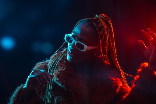 A portrait of an African young woman with braids wearing a coat posing under red and blue neon lights