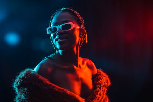 A portrait of an African young woman with braids wearing a coat posing under red and blue neon lights