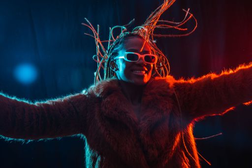 A portrait of an African young woman with braids wearing a coat dancing under red and blue neon lights