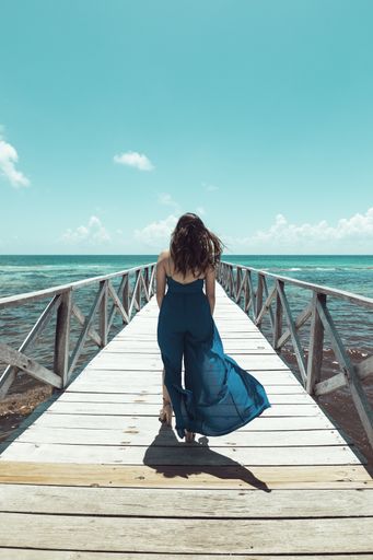 A vertical shot of a gorgeous female walking on a pier in the background of a calm sea