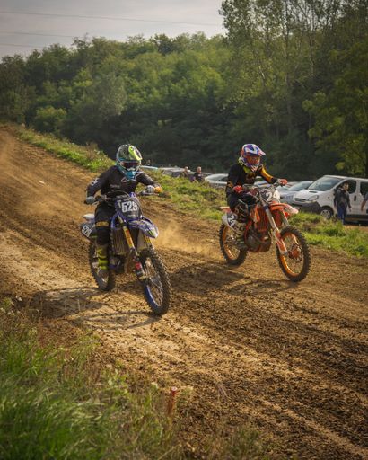 A vertical shot of two sportsmen riding at an off-road motorcycle racing, motocross
