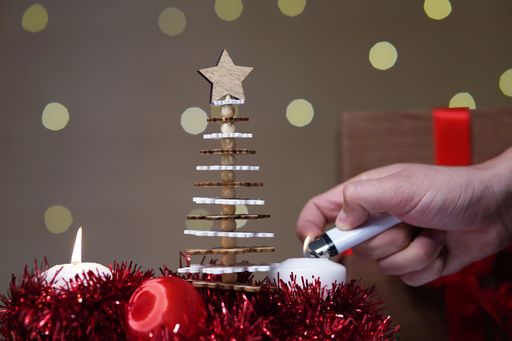 A closeup of red Christmas decorations with a person lighting up the candles and brown background