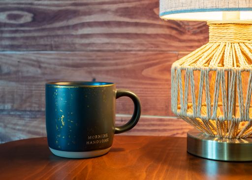 A black coffee cup on a wooden table with a lantern next to it