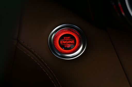 A Mercedes AMG Engine Start Stop button turned on, red, in brown leather with chrome border