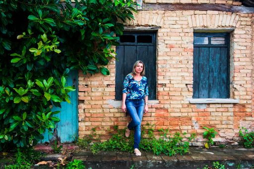 Woman leaning against a window of an old house. Brick facade and leaves around. Aratuipe, Bahia.