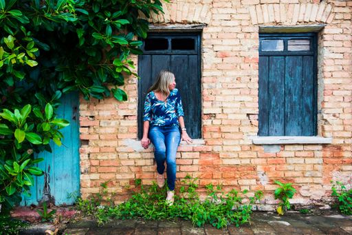 Woman leaning against a window of an old house. Brick facade and leaves around. Aratuipe, Bahia.