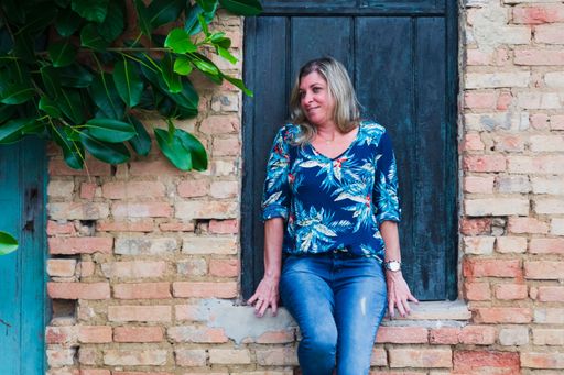 Woman leaning against a window of an old house. Brick facade and leaves around. Aratuipe, Bahia.